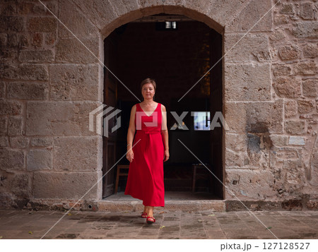 Woman in red dress walking narrow streets of old town Antalya during warm summer evening. Historic atmosphere and Mediterranean charm creates peaceful travel experience. near old mosque 127128527