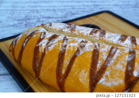Close-up of a sweet mocha golden loaf with chocolate drizzle and powdered sugar on a wooden board. Close-up of a sweet mocha golden loaf with chocolate drizzle and powdered sugar on a wooden board. 127131323