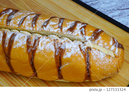 Close-up of a sweet mocha golden loaf with chocolate drizzle and powdered sugar on a wooden board. Close-up of a sweet mocha golden loaf with chocolate drizzle and powdered sugar on a wooden board. 127131324