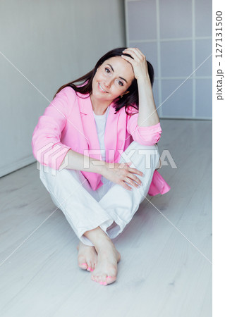 Beautiful brunette woman in white clothes and pink jacket sitting on the floor 127131500