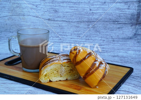A sliced mocha golden loaf with chocolate drizzle and powdered sugar, served with a glass of hot chocolate on a wooden board. A sliced mocha golden loaf with chocolate drizzle and powdered sugar, served with a glass of hot chocolate on a wooden board. 127131649