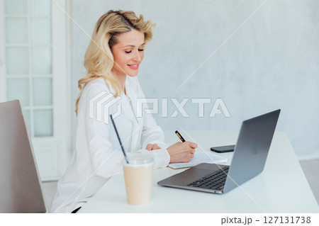 Blonde woman working on laptop at desk in office online Blonde woman working on laptop at desk in office online 127131738