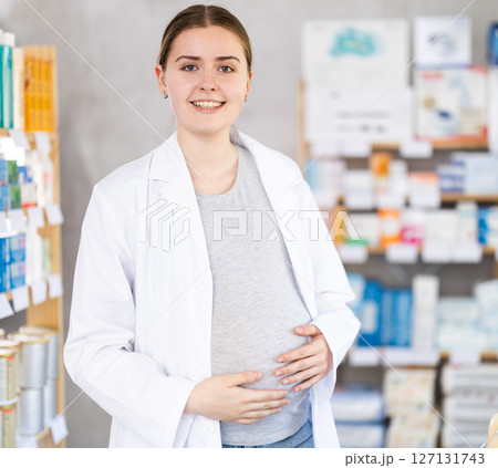 Young pregnant pharmacist welcoming clients in chemist's shop Young pregnant pharmacist welcoming clients in chemist's shop 127131743