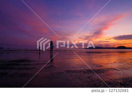 People stroll along the beach and watch the beautiful sunset. 127132081
