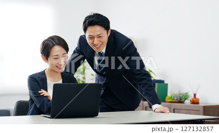 オフィスでノートパソコンを見ながら会話する男女ビジネスパーソンのグループ 127132857