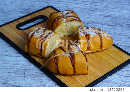 Pieces of a sweet mocha golden loaf with chocolate drizzle and powdered sugar on a wooden board. 127132954