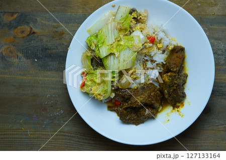 A plate of rice with beef rendang and stir-fried napa cabbage on a wooden table. 127133164