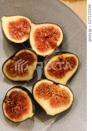 a vertical photo of close up of half cross section of six pieces of fig on a plate 127133356