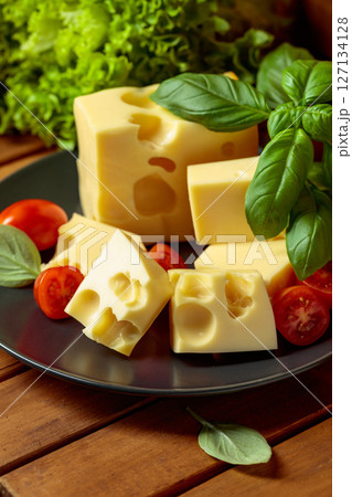 Swiss cheese, green basil, salad, and tomatoes on a wooden table. 127134128