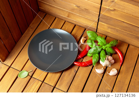 Empty black plate, garlic, basil, and red pepper on a natural wooden background. 127134136