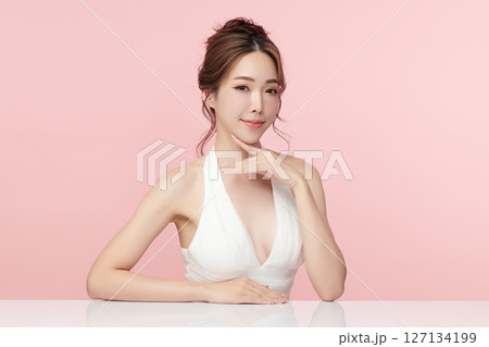 A beautiful young Asian woman with clean, fresh skin against a pink background. Skincare, facial treatment, cosmetology, beauty, and spa. An elegant portrait of an Asian woman. 127134199