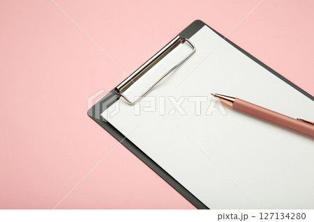 Black tablet with piece of empty paper and pen on pink background. Black tablet with piece of empty paper and pen on pink background. 127134280