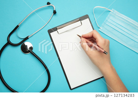 A female hand hold a pen and black clipboard with modern stethoscope, space for messages A female hand hold a pen and black clipboard with modern stethoscope, space for messages 127134283