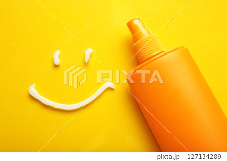 Sunscreen on yellow background. Plastic bottle of sun protection and white cream in the shape of Smiley, smiling face. Sunscreen on yellow background. Plastic bottle of sun protection and white cream in the shape of Smiley, smiling face. 127134289