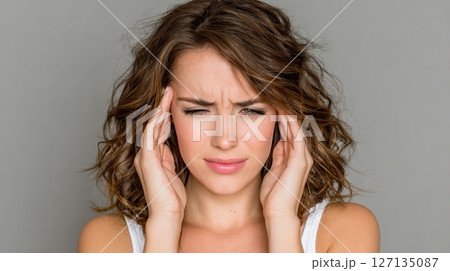 A young woman experiences a headache, and she is trying to relieve her pain by pressing her fingers on her temples. This image focuses on discomfort and possible migraine 127135087