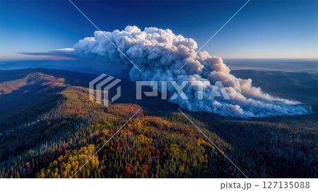 An aerial perspective reveals a wildfire's smoke plume billowing above an autumn forest, displaying the environmental impact on nature with a blue sky backdrop An aerial perspective reveals a wildfire's smoke plume billowing above an autumn forest, displaying the environmental impact on nature with a blue sky backdrop 127135088