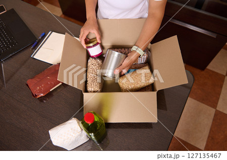 Hands Preparing a Box of Non-Perishable Foods and Essentials 127135467