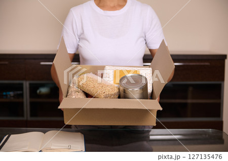 Woman Holding a Box of Food Supplies Including Canned Goods and Grains Woman Holding a Box of Food Supplies Including Canned Goods and Grains 127135476