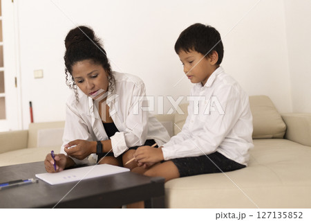 Babysitter helping child with homework on sofa at home 127135852
