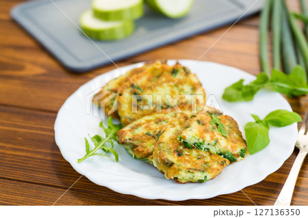 breakfast of zucchini fritters with green onions in a plate on a wooden table 127136350