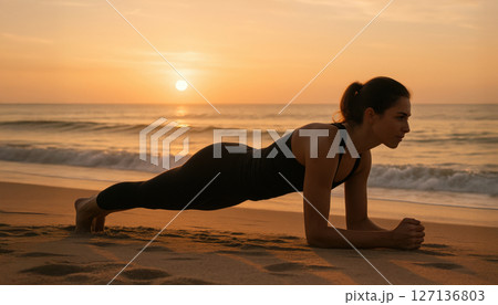 Focused young woman holding plank position on sandy beach at sunrise, training core strength by the ocean. Early morning fitness discipline. Wellness and determination. Focused young woman holding plank position on sandy beach at sunrise, training core strength by the ocean. Early morning fitness discipline. Wellness and determination. 127136803