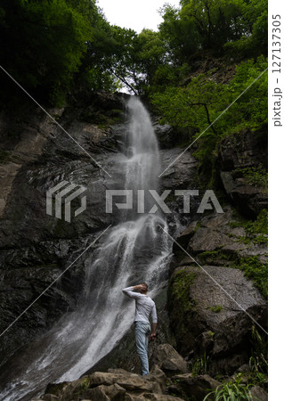A man looks at a waterfall in the mountains in surprise. Waterfall in Georgia 127137305