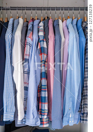 Neatly arranged men shirts hanging on wooden hangers in wardrobe. Minimalist clothing organization and classic male fashion concept Neatly arranged men shirts hanging on wooden hangers in wardrobe. Minimalist clothing organization and classic male fashion concept 127138239
