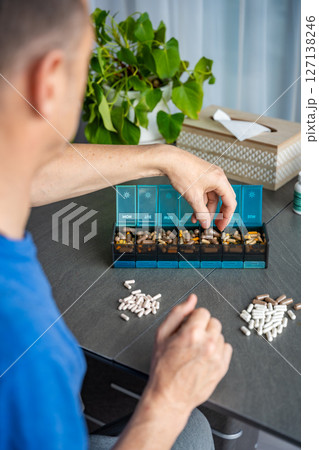 Man sorting his pills and supplements into a weekly pill organizer. Concept of medication management and daily health routine Man sorting his pills and supplements into a weekly pill organizer. Concept of medication management and daily health routine 127138246