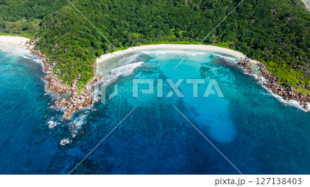 Waves wash up against the shore with a vibrant green forest in the background. Anse Cocos beach. La Digue, Seychelles. Waves wash up against the shore with a vibrant green forest in the background. Anse Cocos beach. La Digue, Seychelles. 127138403