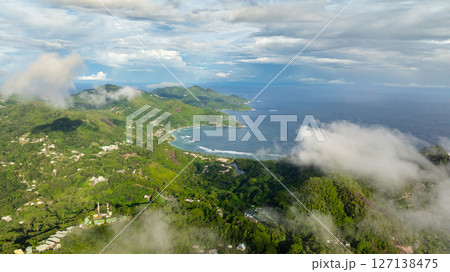 Mountainous green coastline with patches of mist, meeting the turquoise ocean. Seychelles, Mahe. 127138475