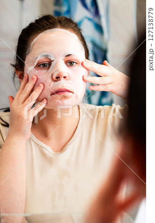 Female applying moisturizing face mask in bathroom. Beauty routine. International Self Care Day. 127138779
