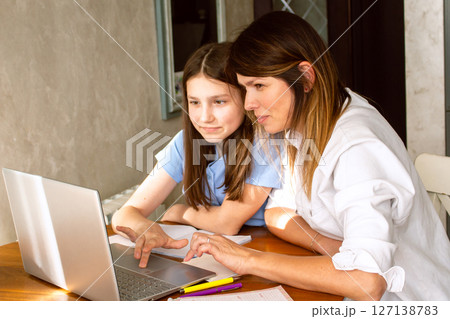 Mom and daughter surfing internet on laptop sitting in kitchen, online shopping. Watching something exciting on internet. Mom and daughter surfing internet on laptop sitting in kitchen, online shopping. Watching something exciting on internet. 127138783