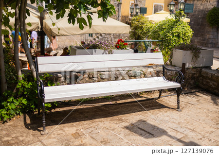 Empty bench under green trees on a sunny day. Relaxation, summer mood, and peaceful outdoor atmosphere. 127139076