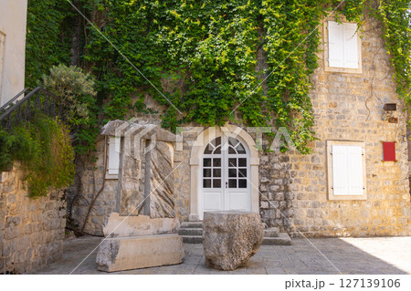 Ancient stone sculpture near ivy-covered historical building. Urban greenery, cultural heritage, and Mediterranean architecture. Ancient stone sculpture near ivy-covered historical building. Urban greenery, cultural heritage, and Mediterranean architecture. 127139106