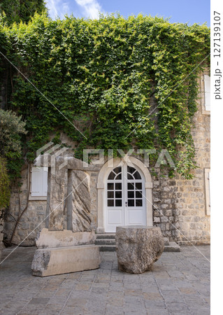 Ancient stone sculpture near ivy-covered historical building. Urban greenery, cultural heritage, and Mediterranean architecture. Ancient stone sculpture near ivy-covered historical building. Urban greenery, cultural heritage, and Mediterranean architecture. 127139107