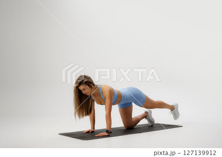 Woman performing an exercise routine on a mat in a studio during daylight hours for fitness and health Woman performing an exercise routine on a mat in a studio during daylight hours for fitness and health 127139912