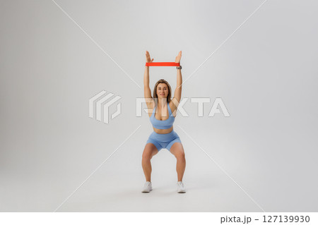 Woman performs a strength training exercise with a resistance band in a minimalist indoor space Woman performs a strength training exercise with a resistance band in a minimalist indoor space 127139930