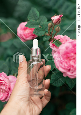 Natural beauty product showcased with elegance: serum in hand amid blooming roses, promoting self-care and floral aesthetics. 127140107
