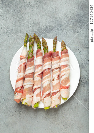 Fresh asparagus wrapped in bacon with peppercorns on gray concrete background top view 127140434