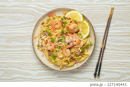 Pad thai noodles with shrimps and chopsticks on white wooden table, traditional dish of Thailand Pad thai noodles with shrimps and chopsticks on white wooden table, traditional dish of Thailand 127140441