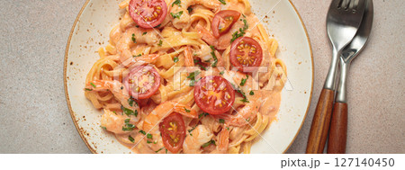 Seafood pasta linguine with shrimps and cherry tomatoes in creamy sauce garnished with parsley on white plate on light warm beige background top view 127140450