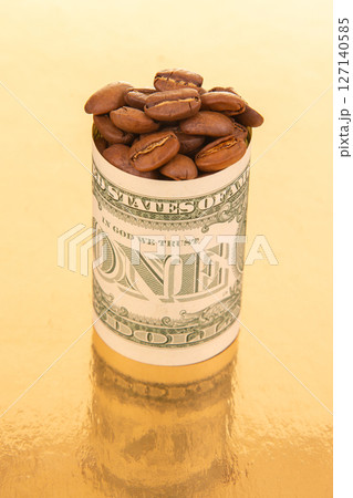 A minimalist scene with a rolled one-dollar bill holding coffee beans on a gold surface 127140585