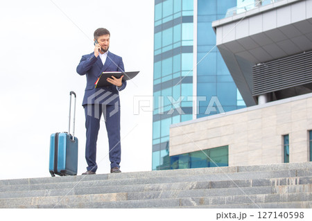 business man stands with a travel suitcase on the steps against the background of an office building 127140598