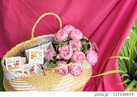 Wicker basket filled with natural cosmetic boxes with creams and roses, bright pink fabric background. Concept of natural skin care, eco and floral inspiration. Rosa damascena. Rose production season 127140639