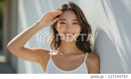 白い壁の前で日差しを避ける笑顔の女性 127144783