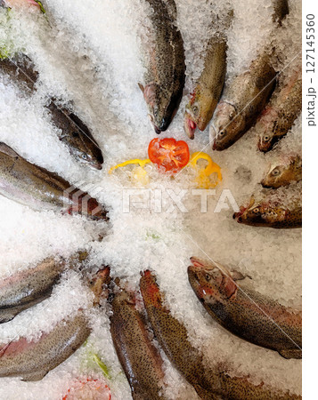 freshly chilled trout arranged on ice with colorful vegetables for seafood market. closeup. freshly chilled trout arranged on ice with colorful vegetables for seafood market. closeup. 127145360