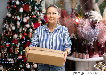 Happy woman holding a cardboard box with Christmas decorations in a store 127148138