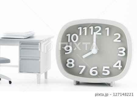 書類の置かれたミニチュアのオフィスの机と8時を指す時計 127148221