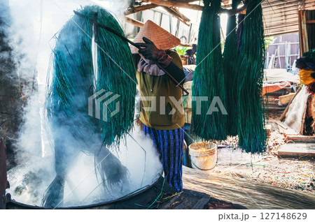 Vietnamese woman in a traditional straw hat dyes reeds at a woven mat factory in Vietnam Vietnamese woman in a traditional straw hat dyes reeds at a woven mat factory in Vietnam 127148629
