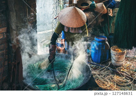 Vietnamese woman in a traditional straw hat dyes reeds at a woven sleeping mat factory in Vietnam Vietnamese woman in a traditional straw hat dyes reeds at a woven sleeping mat factory in Vietnam 127148631